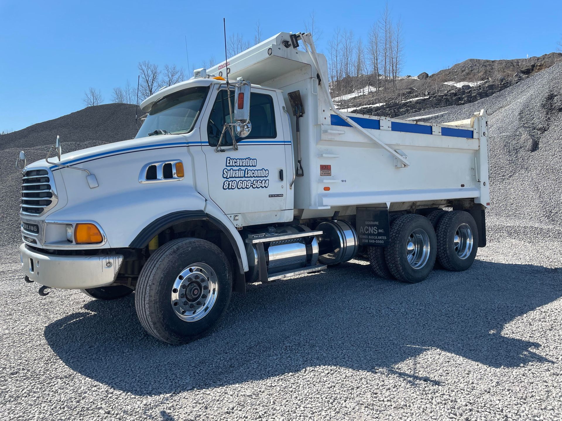 Un camion-benne blanc est garé sur un terrain en gravier.