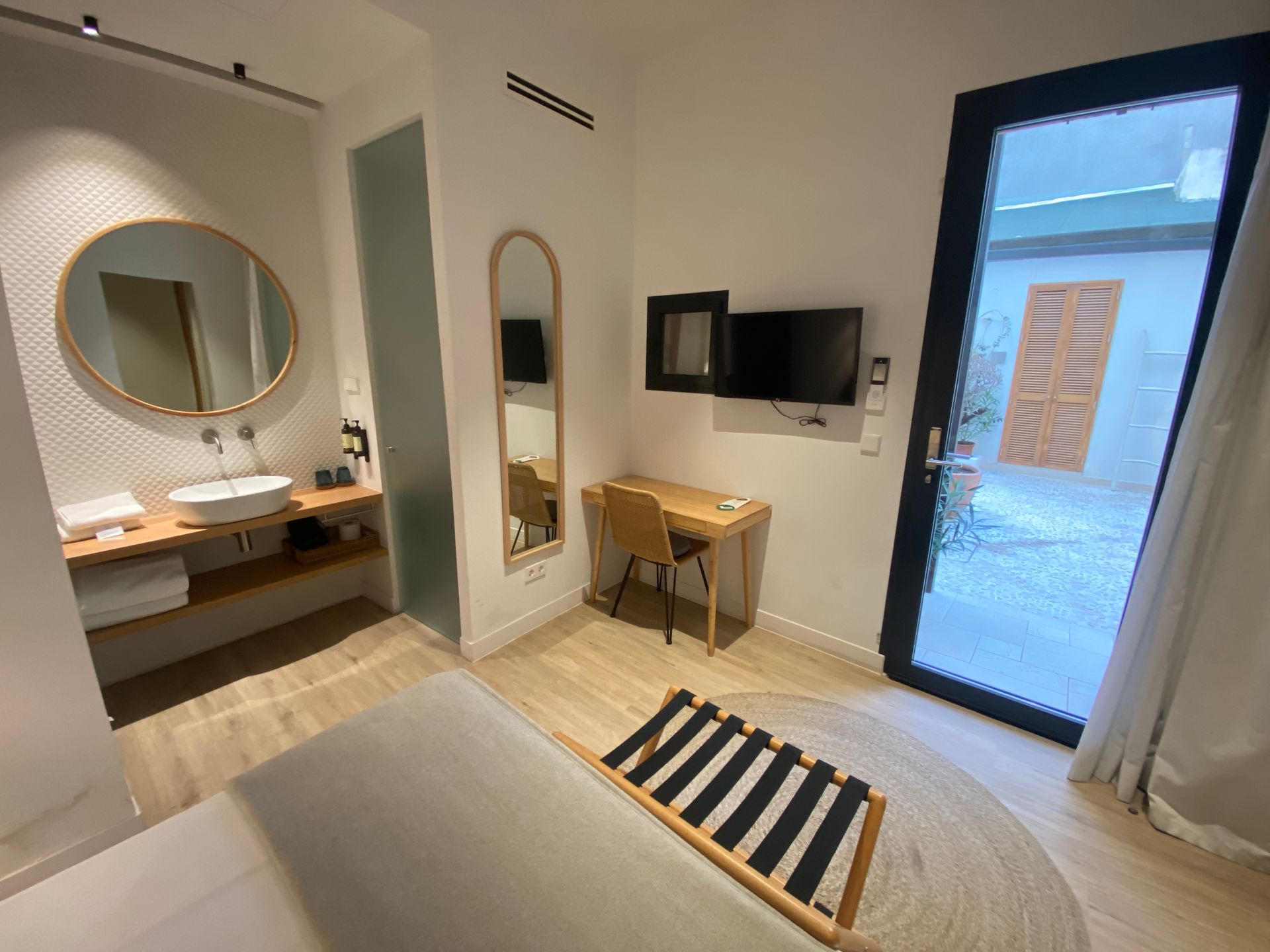 A hotel room with a bed , desk , television , sink and mirror.