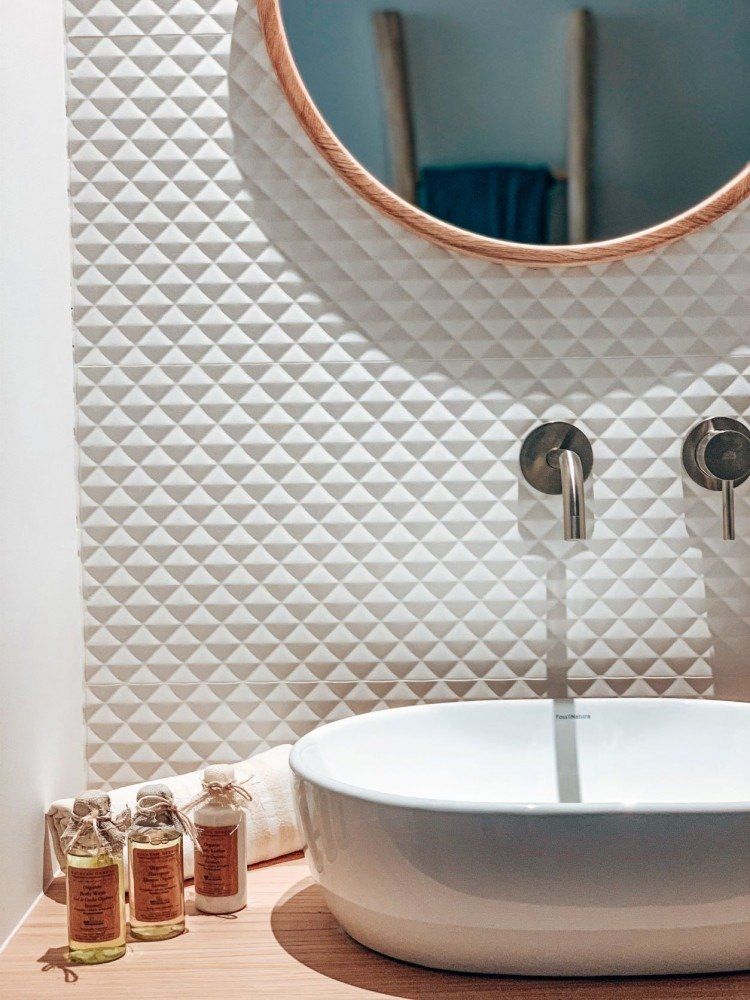 A bathroom with a sink , mirror and bottles of soap.