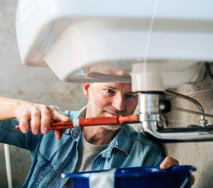 A man is fixing a sink with a wrench. A man is fixing a sink with a wrench.