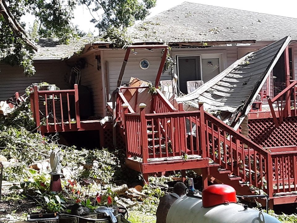 Storm-damaged house with collapsed porch and debris in the yard