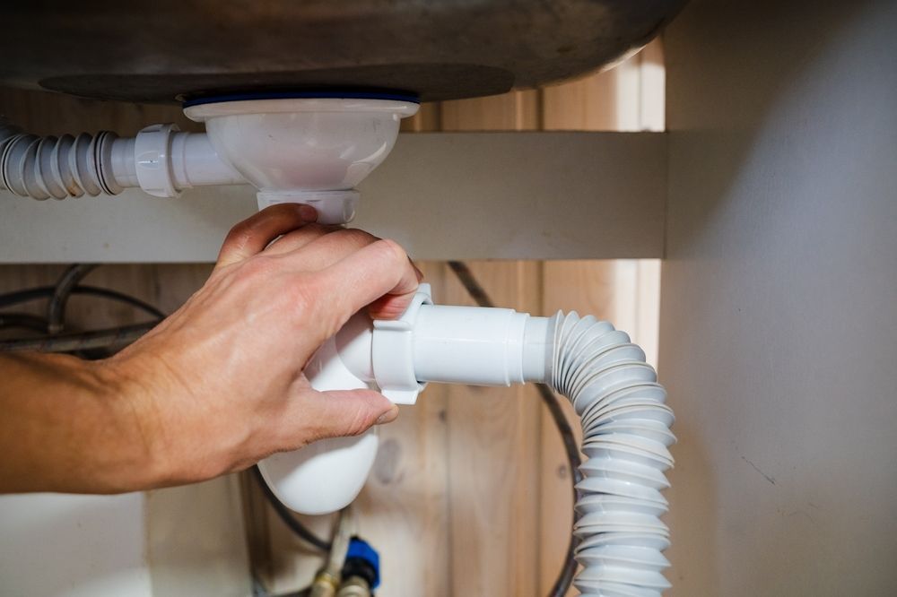 Hand adjusting plumbing under sink