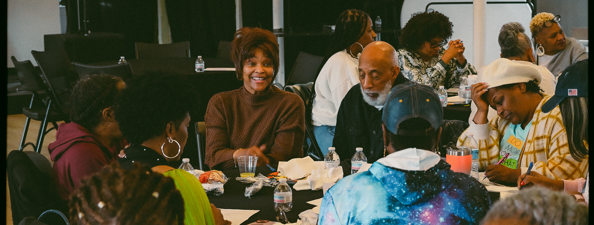 People gathered around a table at a lively indoor meal, with plates, drinks, and colorful decor.