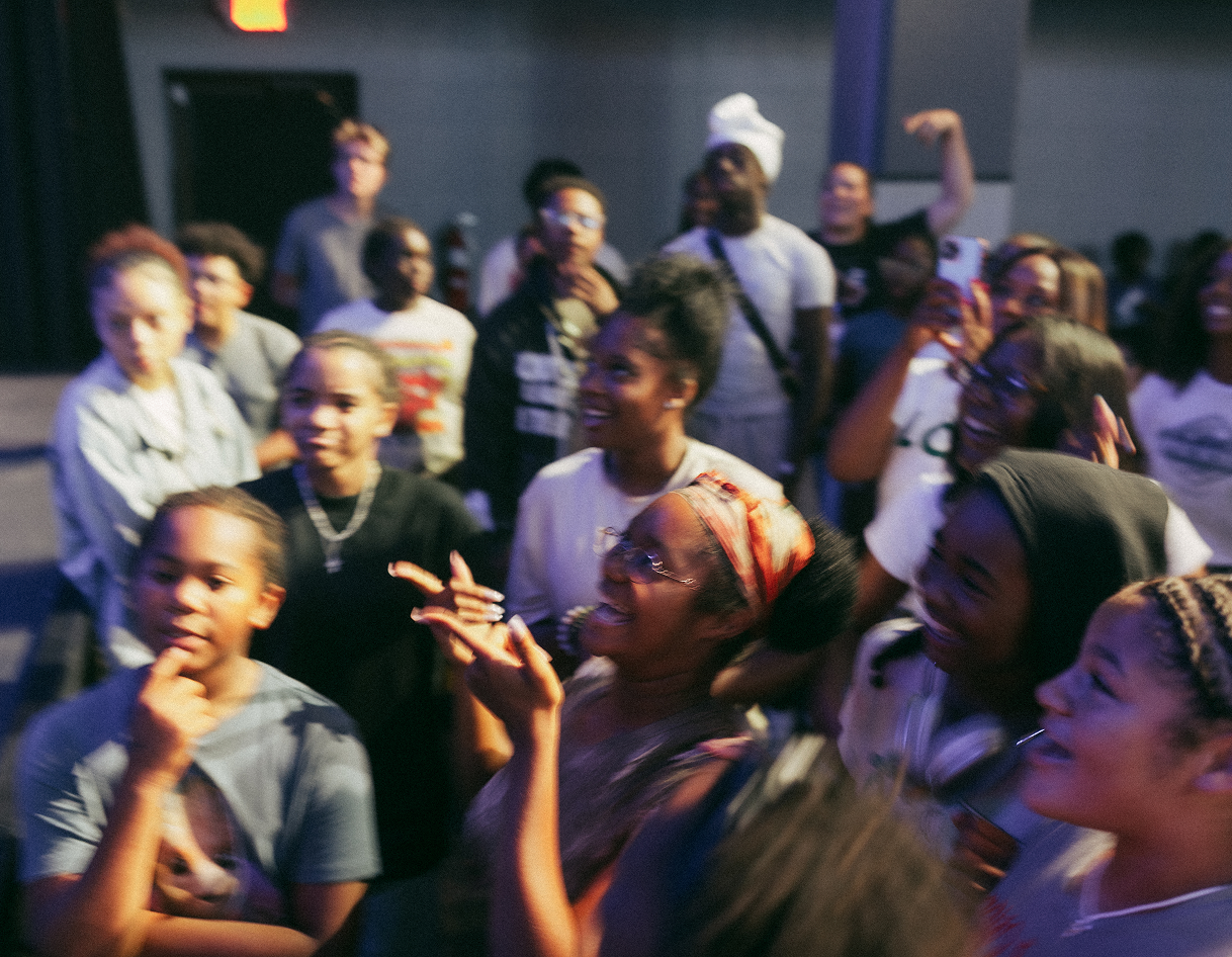 Crowd of people cheering and dancing at a lively indoor event under colorful lights