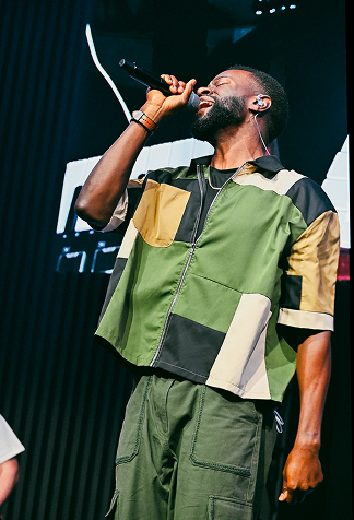 Singer performing on stage in green-and-black outfit, holding a microphone and singing into it