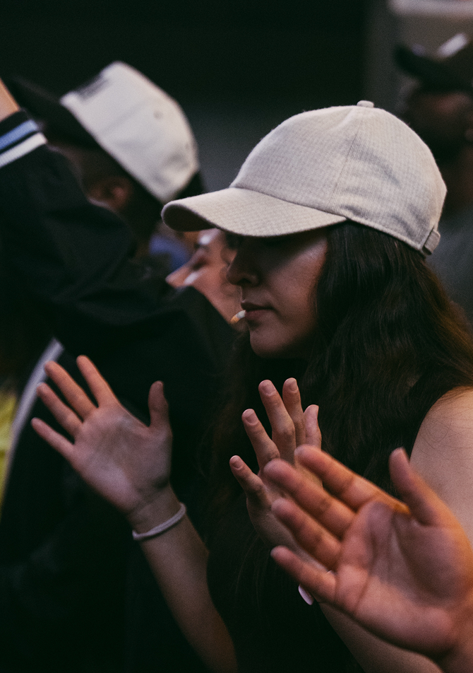 People with raised hands wearing white caps in a dim indoor crowd