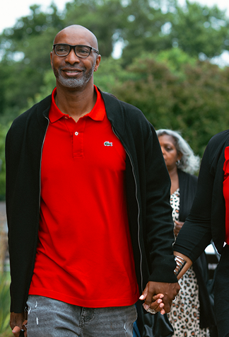 Man in red polo and black jacket walking outdoors, holding hands with someone off-frame.