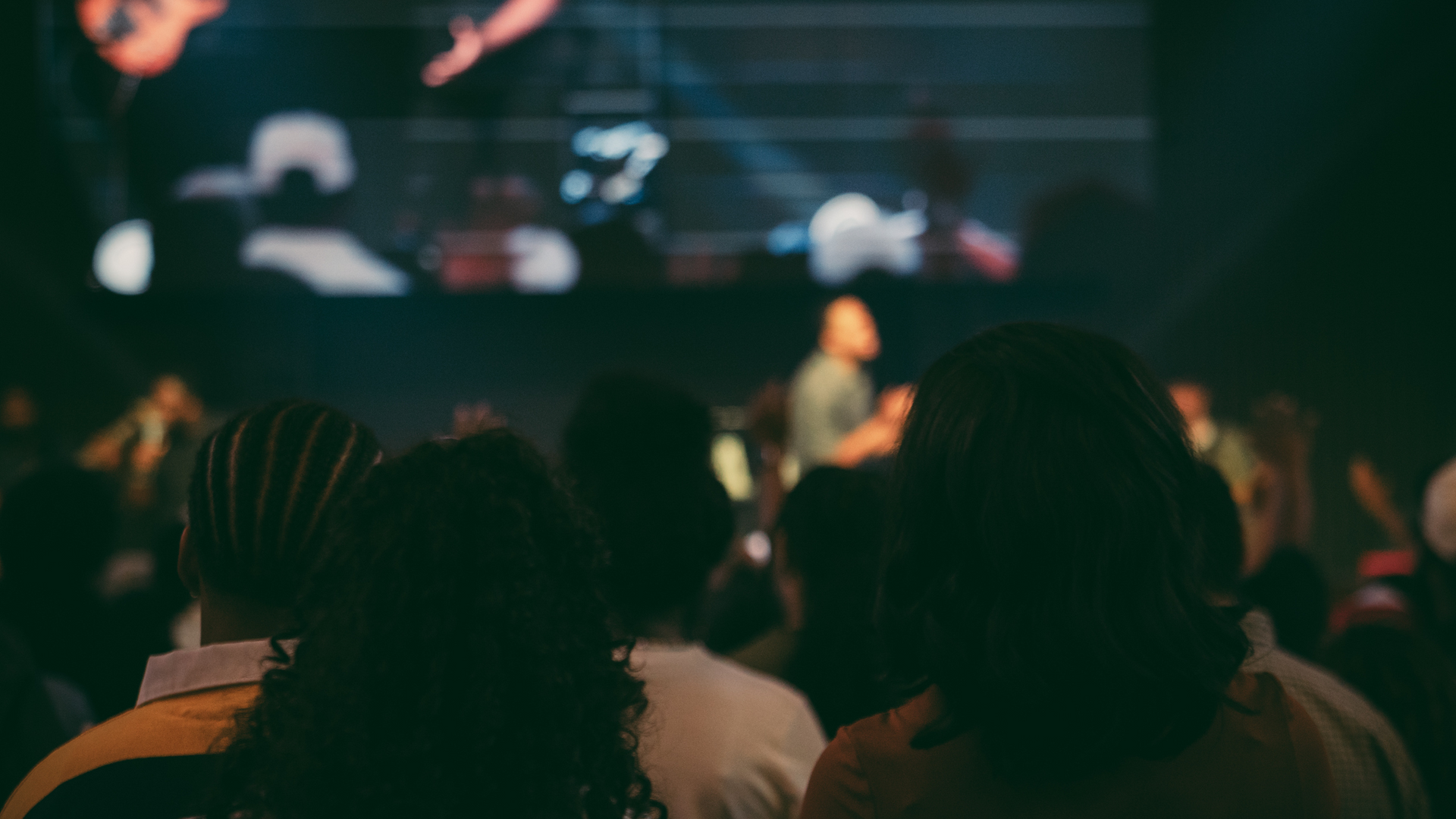 Audience watching a live concert on a dimly lit stage with blurred performers in the background