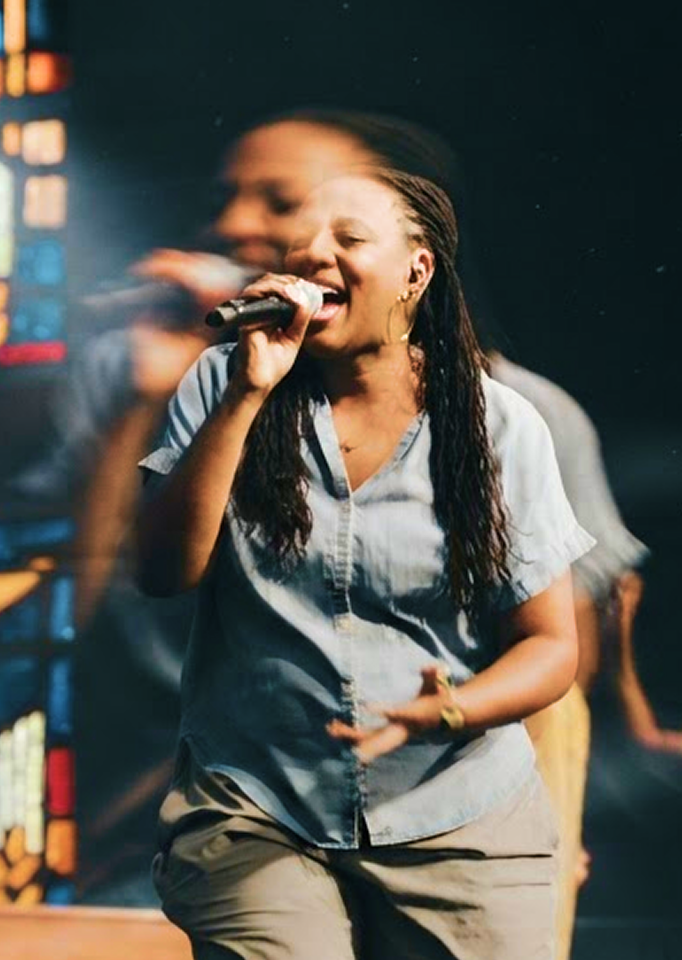 Singer performing on stage, holding a microphone with colorful lights in the background