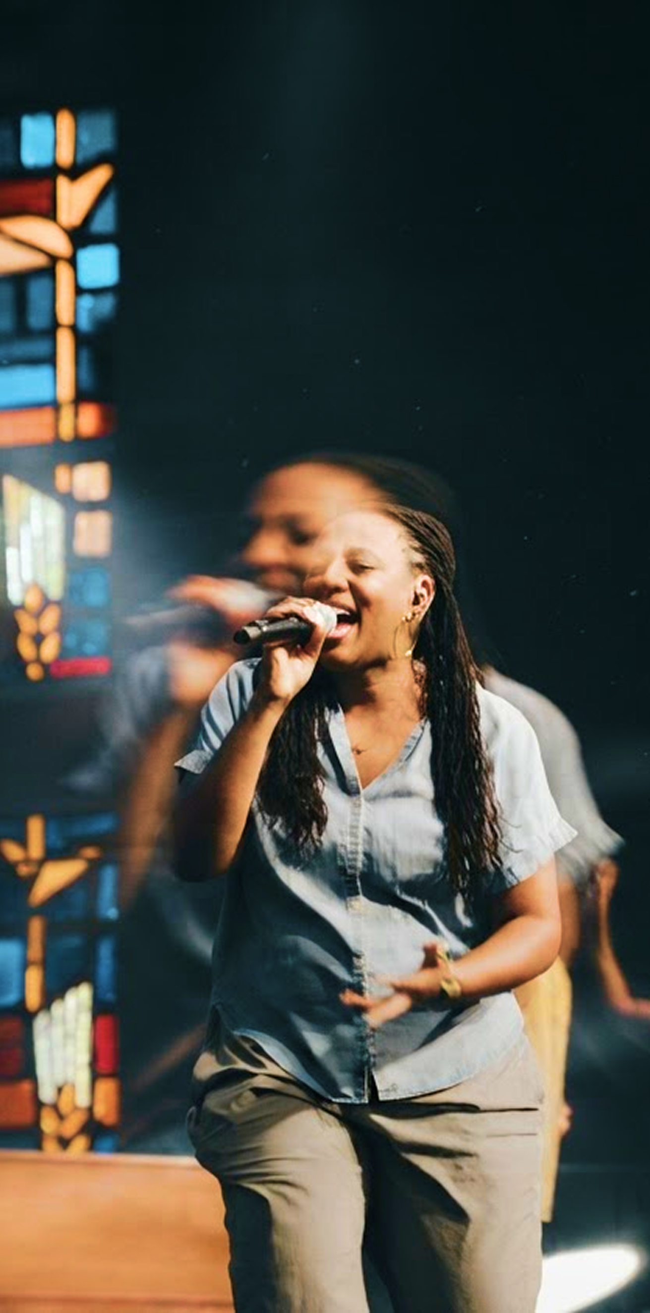 Singer performing on stage, holding a microphone and smiling under colorful lights.