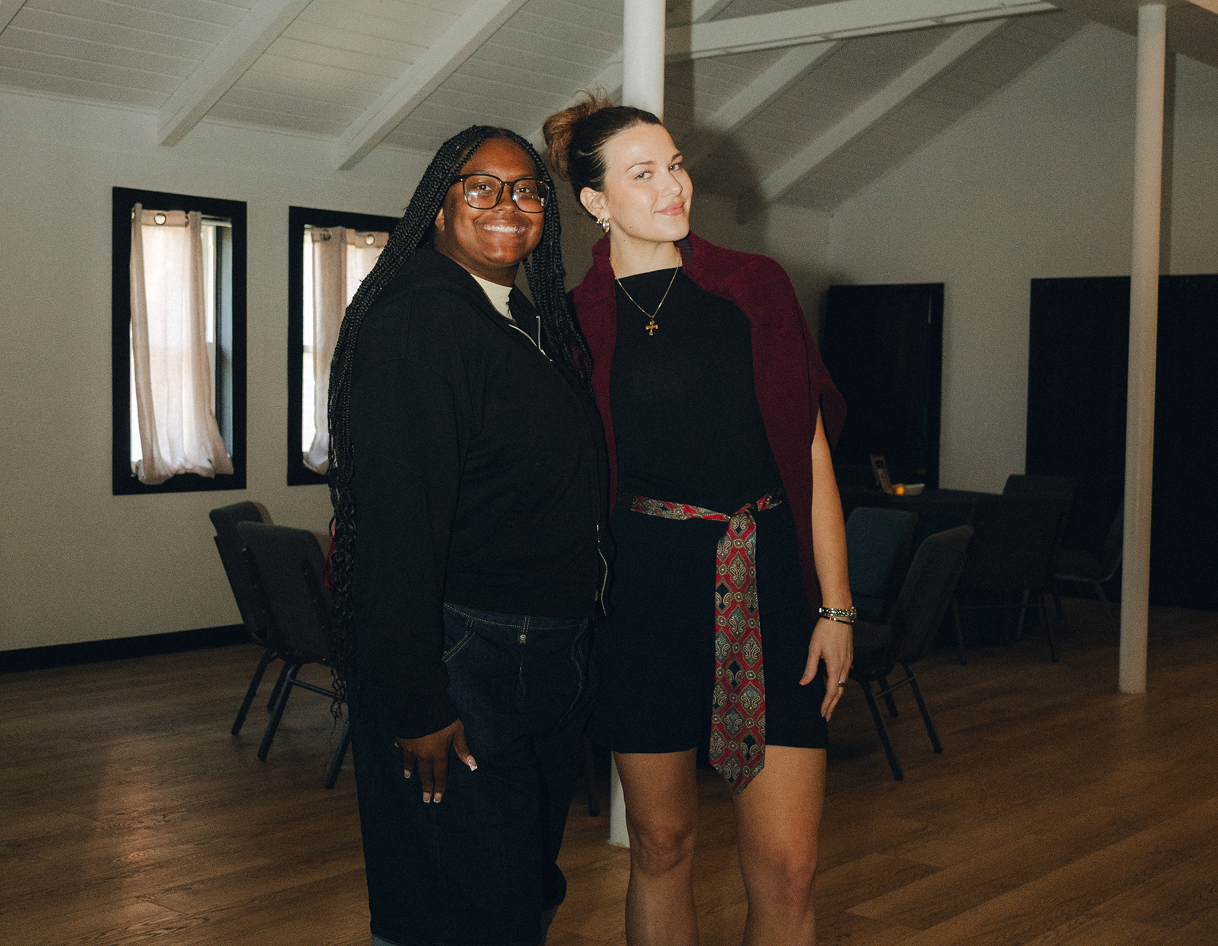 Two people posing together in a spacious room with wood floors and exposed beams