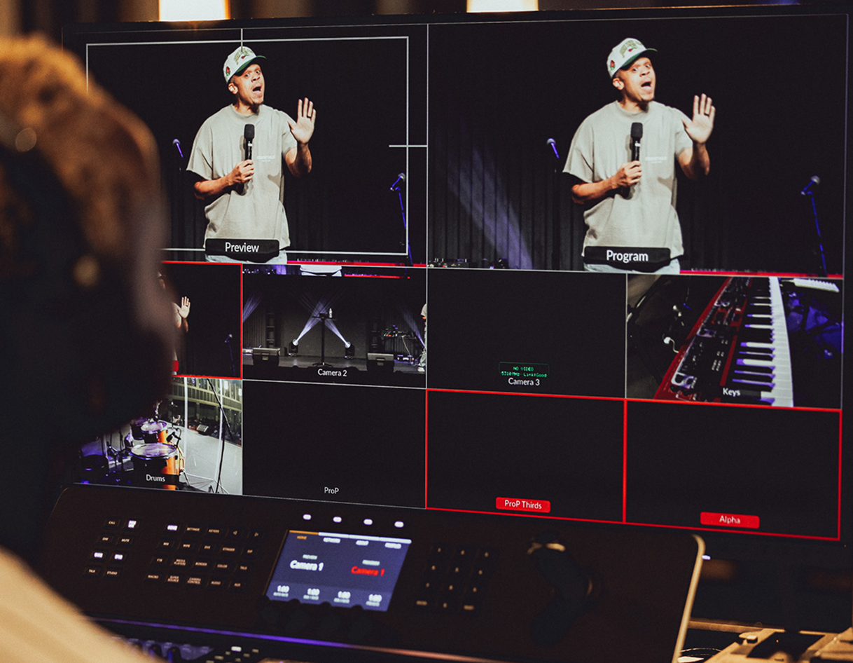 Control room monitors showing a presenter onstage and multiple camera feeds in a live production setup