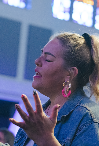 Woman in a denim jacket singing passionately onstage, eyes closed and hand raised.