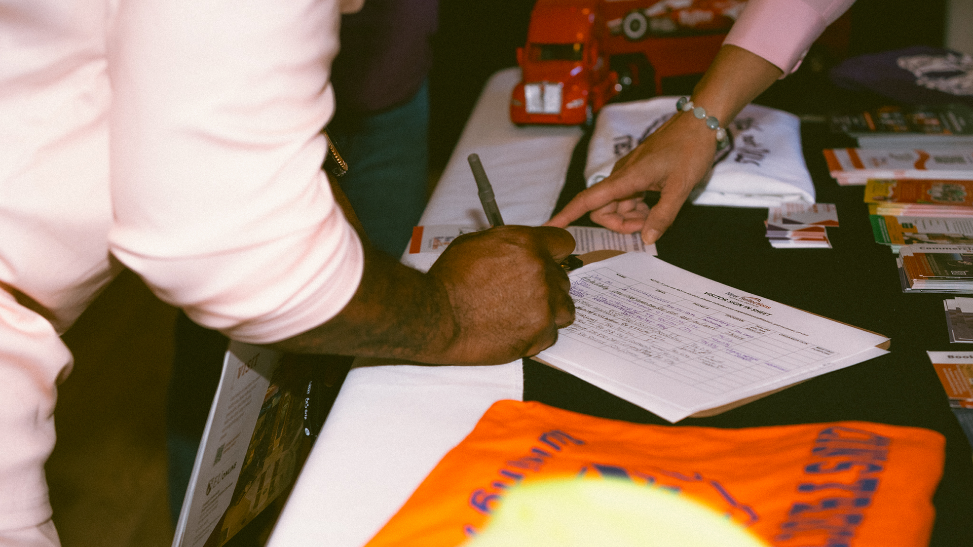 Hands and documents on a table during a meeting, with a bright orange folder in the foreground.