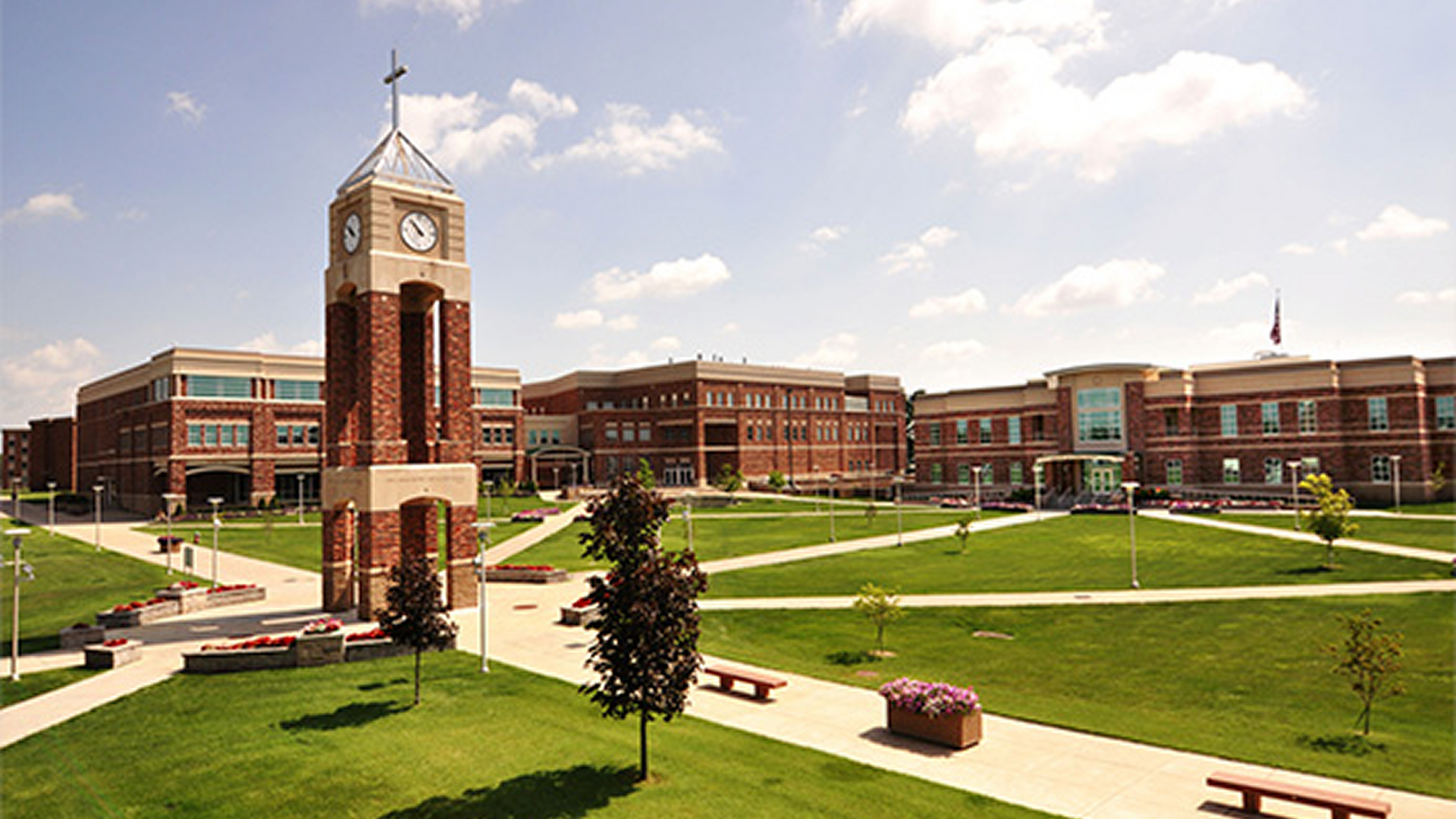Brick campus with clock tower, green lawns, and academic buildings under a partly cloudy sky