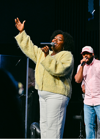 Singer holding a microphone and pointing, performing on stage under blue lighting