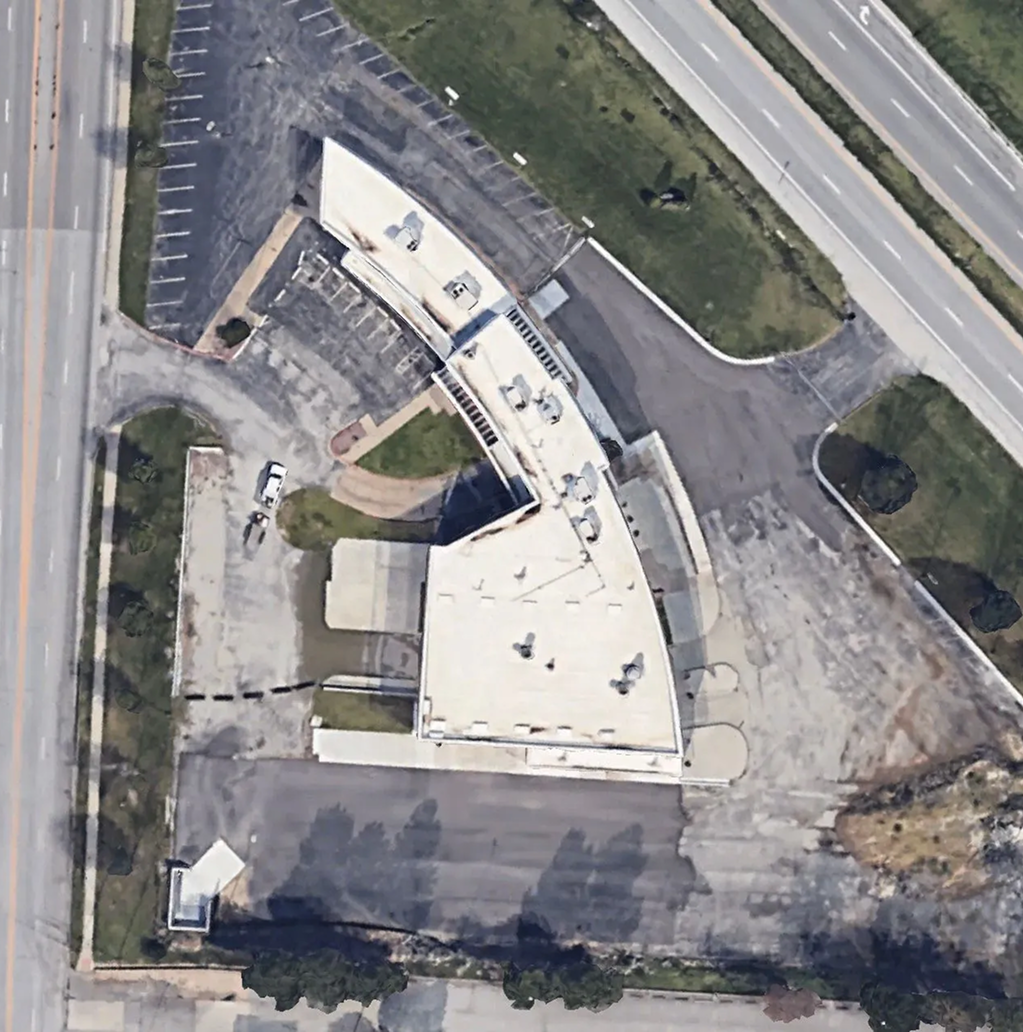 Aerial view of a curved white building with a parking lot and surrounding roads