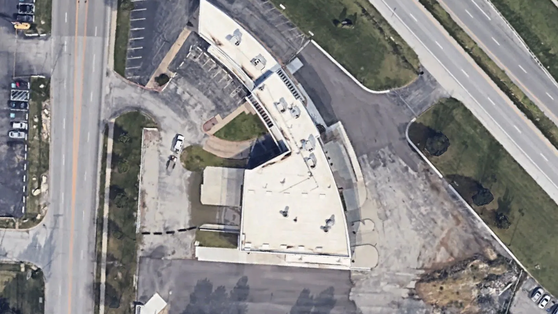 Aerial view of a curved white building with a parking lot and surrounding roads