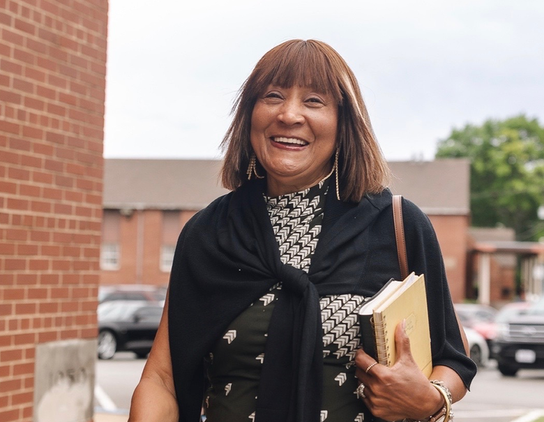 Smiling person holding books outdoors beside a brick building