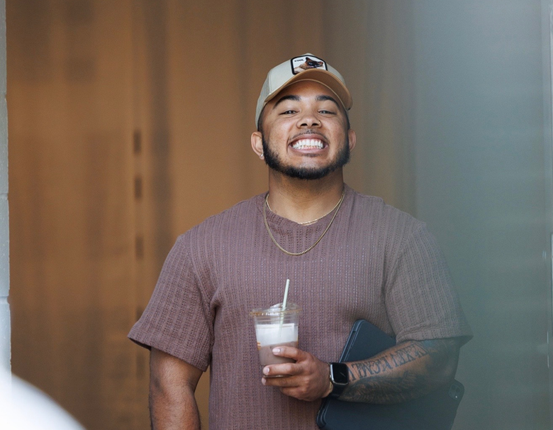 Smiling person in a brown knit shirt holding a drink indoors