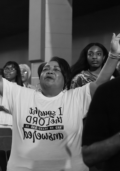 Crowd with raised arms at a public gathering; woman in white T-shirt stands in front.