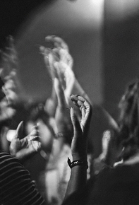 Raised hands clapping at a concert, with blurred stage lights in the background