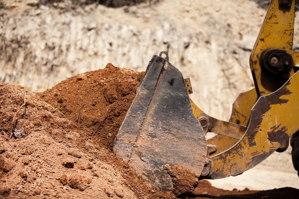 Yellow Excavator Bucket Scoops Up Brown Soil — BC Earthmoving and Tipper Hire in Cooroy, QLD