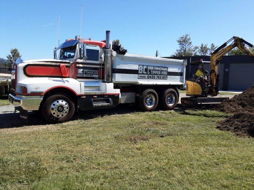 Red Dump Truck Unloading Soil Onto a Grassy Area on a Sunny Day — BC Earthmoving and Tipper Hire in Gympie, QLD