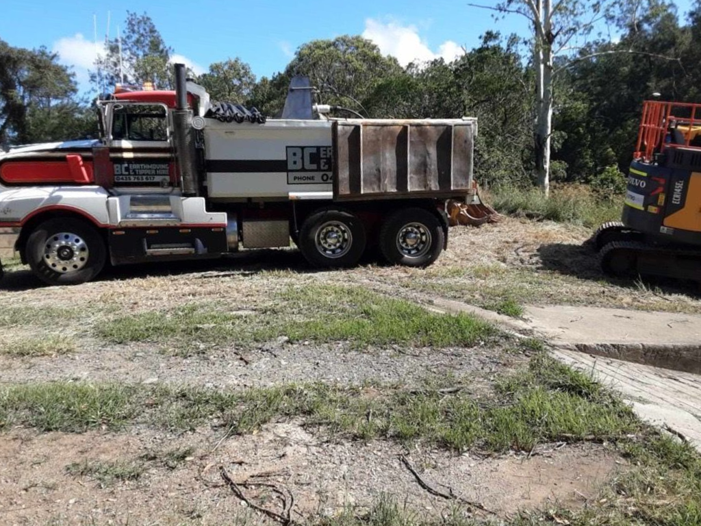 Dump truck and excavator parked on a dirt path with trees in the background under a blue sky — BC Earthmoving and Tipper Hire in Gympie, QLD