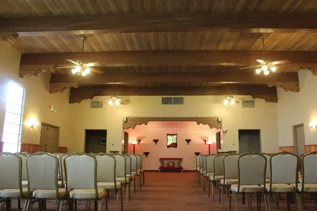 Rows of chairs face a stage in a room with a wooden ceiling and red carpet.