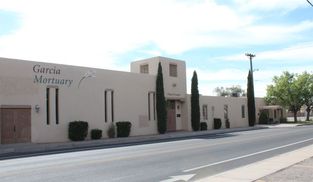 Beige stucco building with bell tower, arched windows, red tile roof, and blue sky.