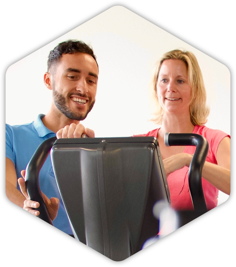 Ein Fitnesstrainer berät eine Frau auf einem Ergometer