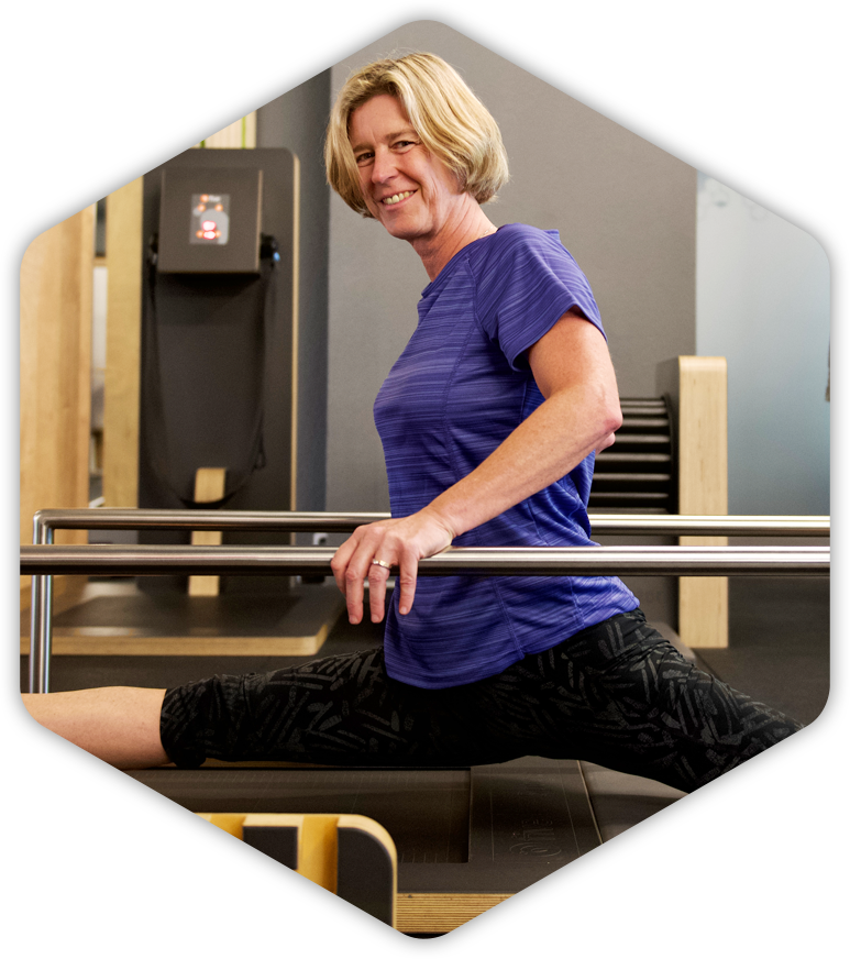 Eine Frau in einem lila Hemd streckt ihre Beine an einer Stange in einem Fitnessstudio