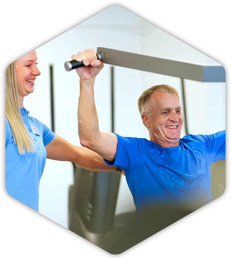 Ein Mann in einem blauen Hemd hebt eine Hantel, während eine Fitnesstrainerin zusieht