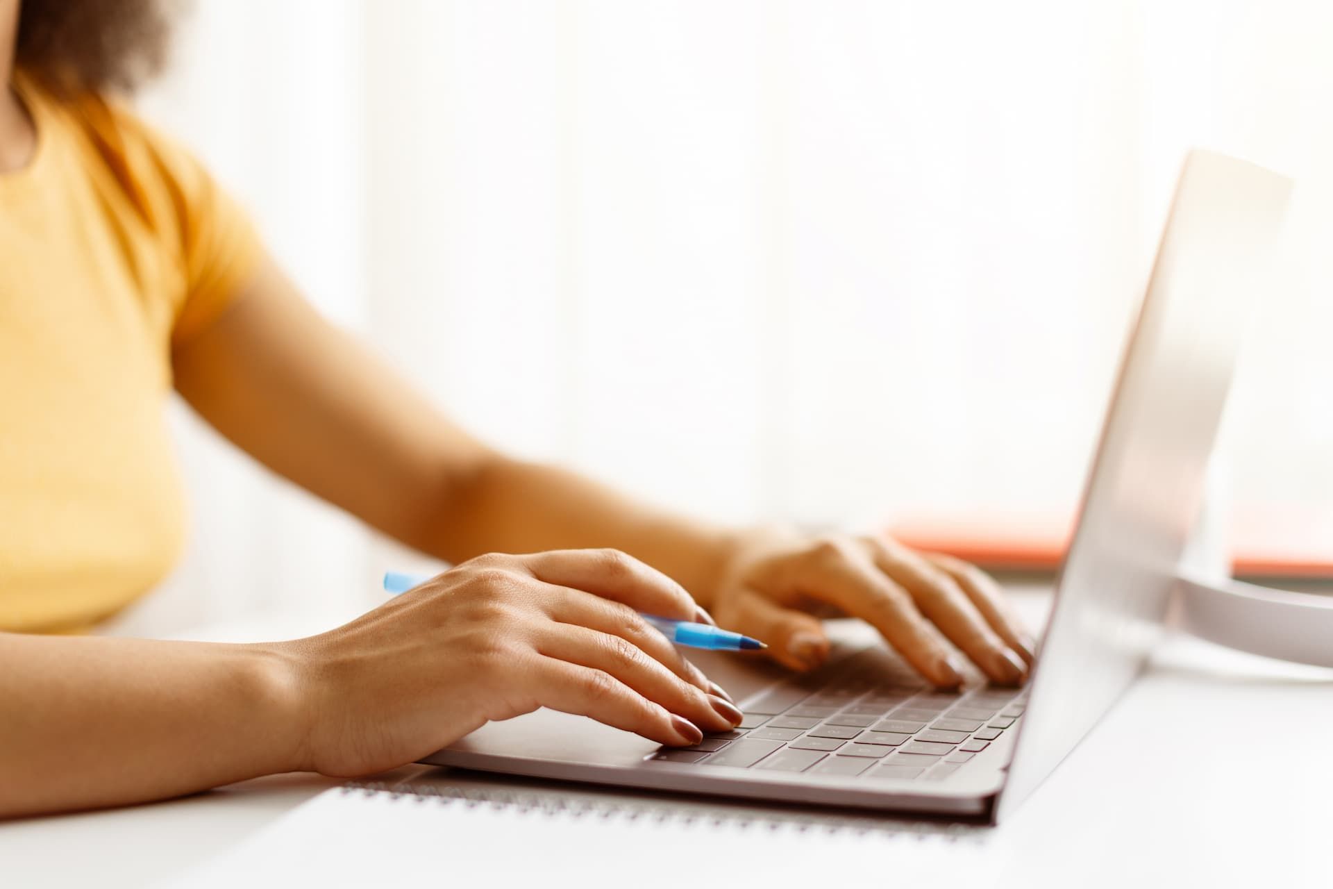 Person typing on a laptop at a bright desk, with hands visible and a white background.