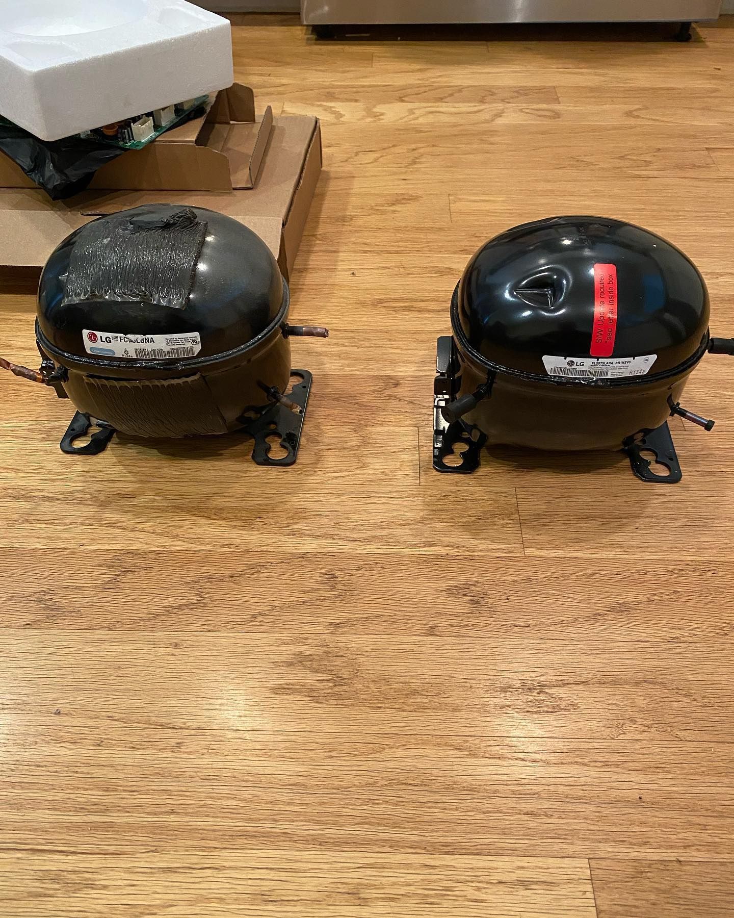 Two compressors are sitting on a wooden floor.