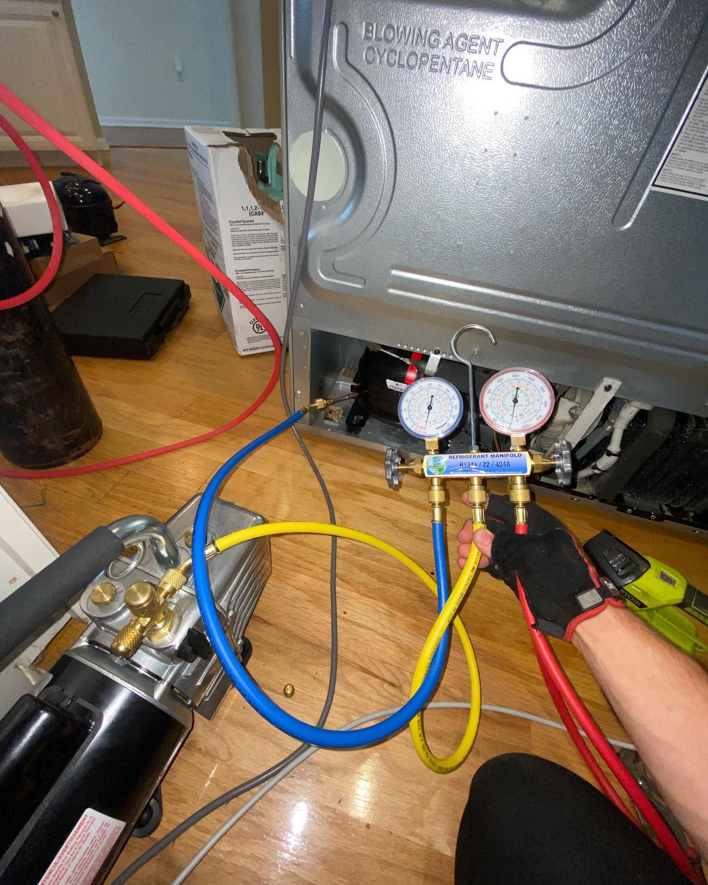 A person is working on a refrigerator with a vacuum pump attached to it.