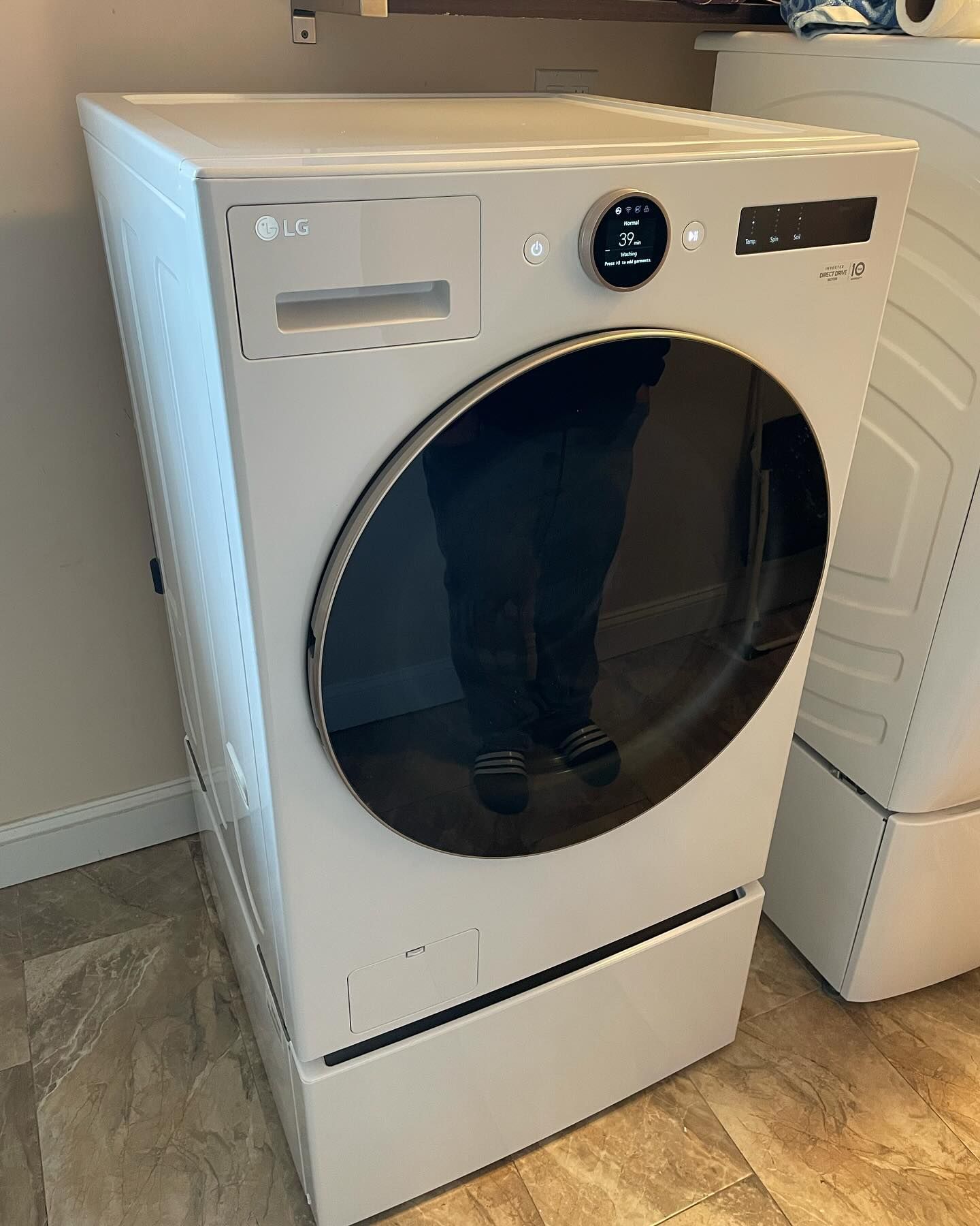 A white lg dryer is sitting on a tiled floor in a laundry room.