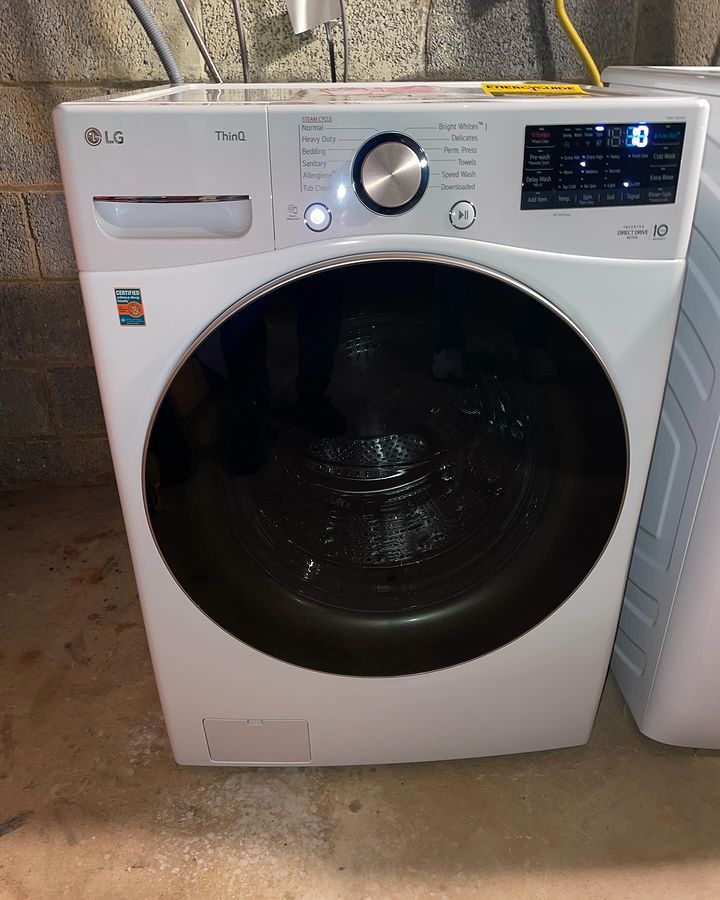 A white lg washing machine is sitting on the floor in a laundry room.