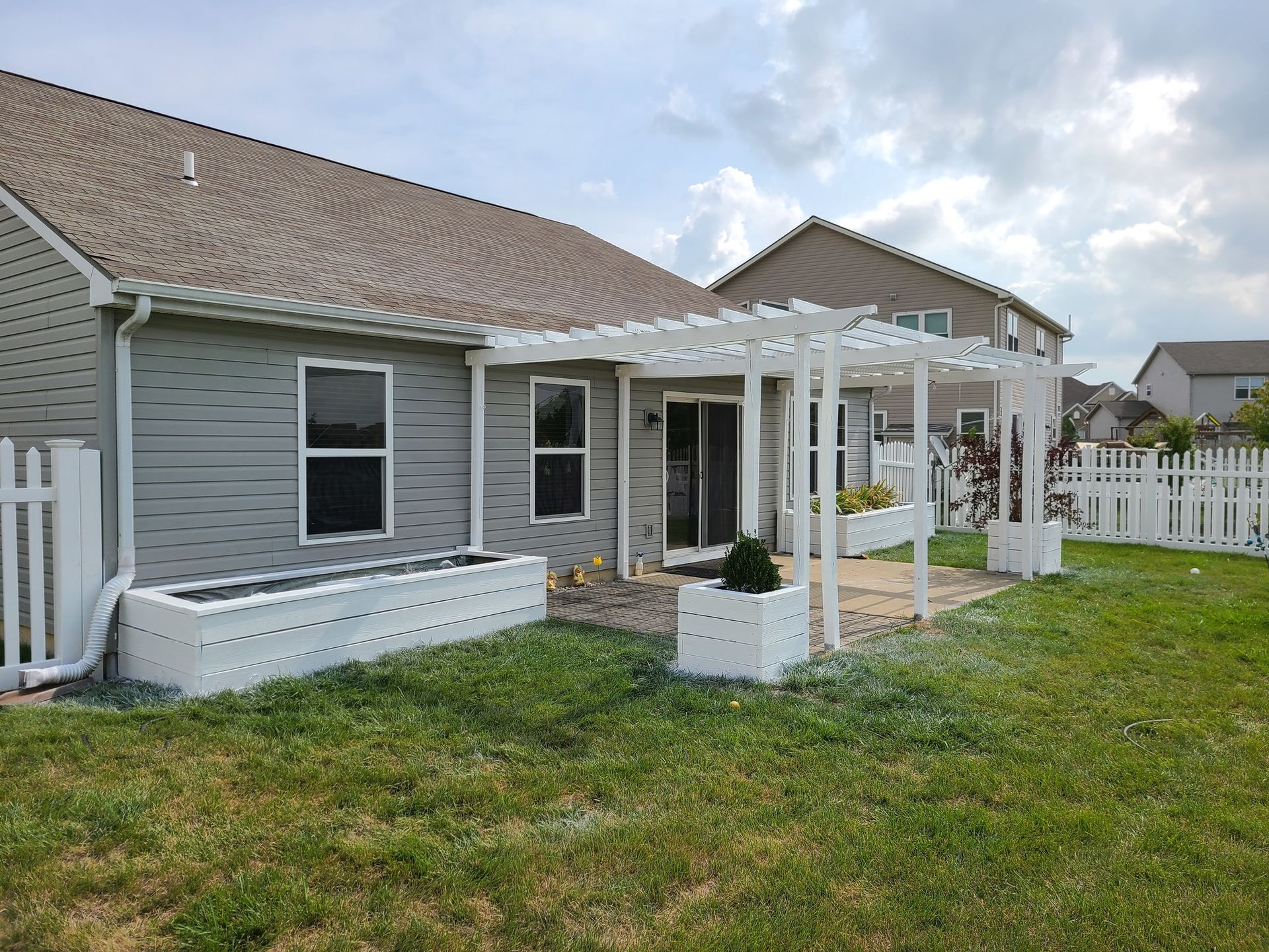The backyard of a house with a pergola and planters.