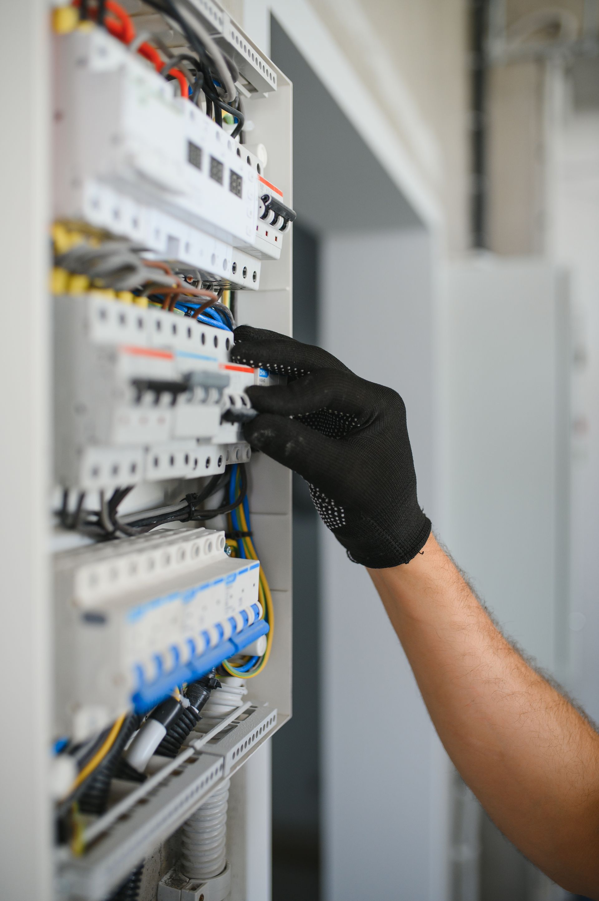 Gloved hand adjusting breakers in an electrical control panel with wires and switches