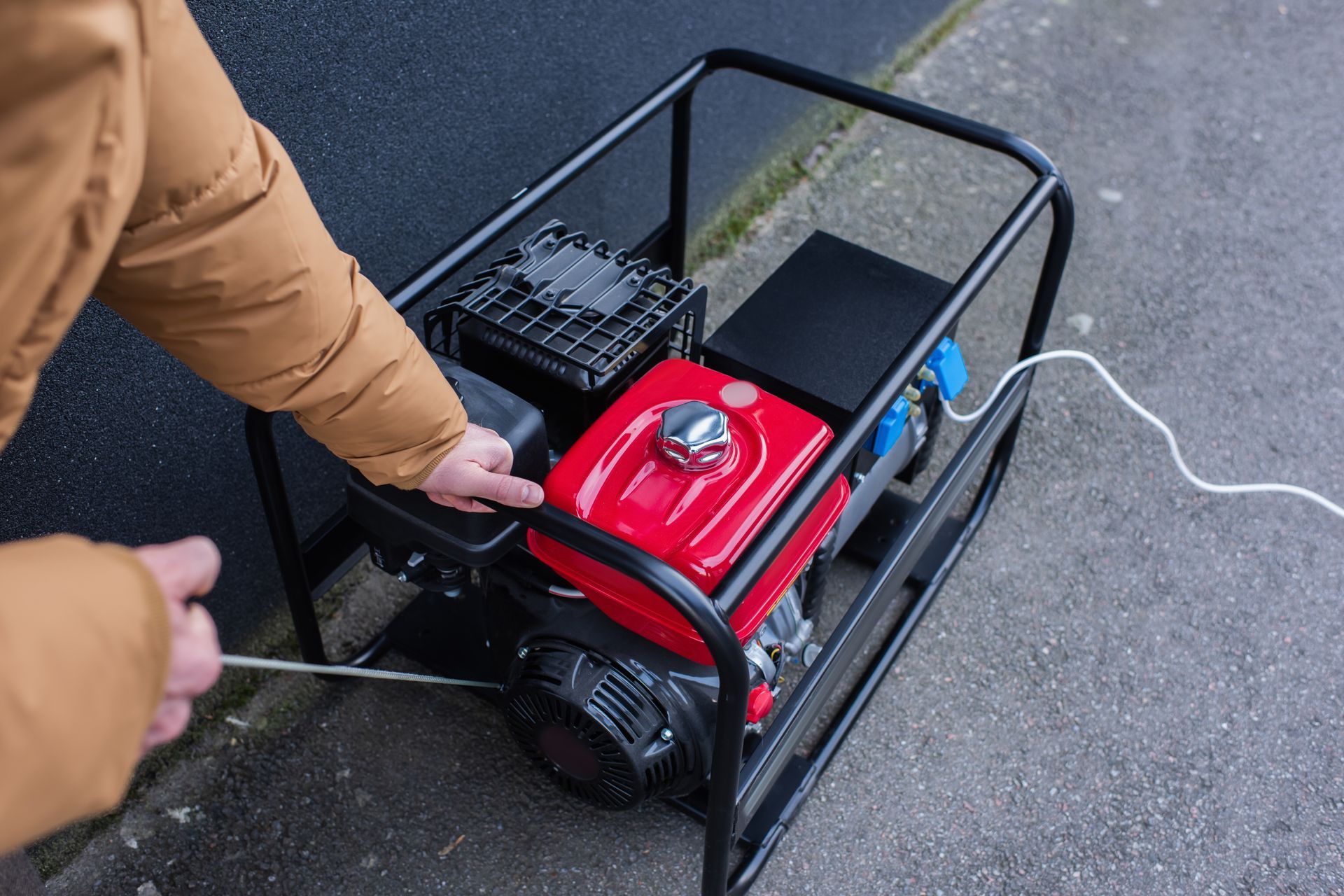 Person starting a red portable generator in a black metal frame outdoors on pavement