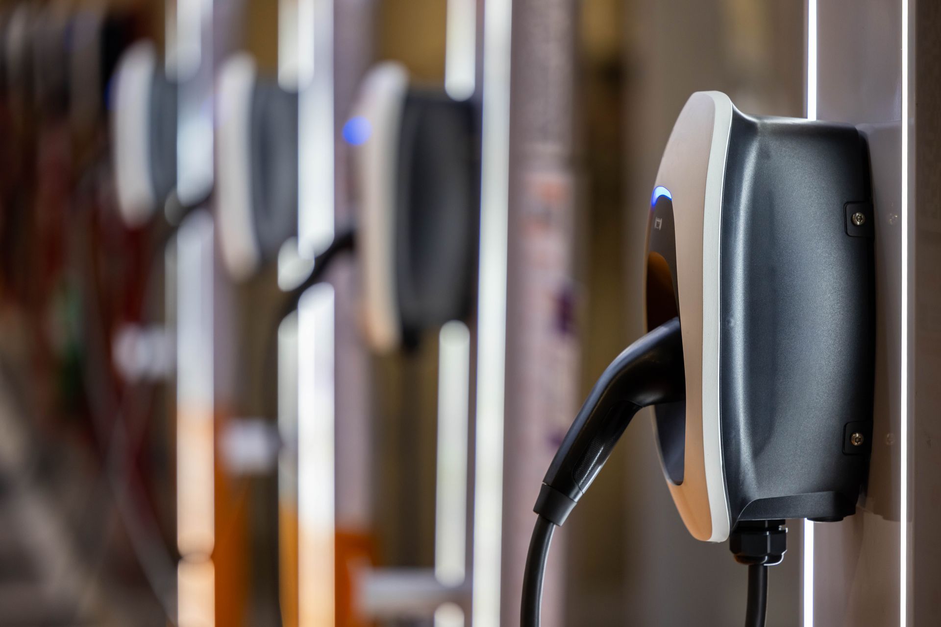 Electric vehicle charging plugs connected to wall-mounted stations in a row