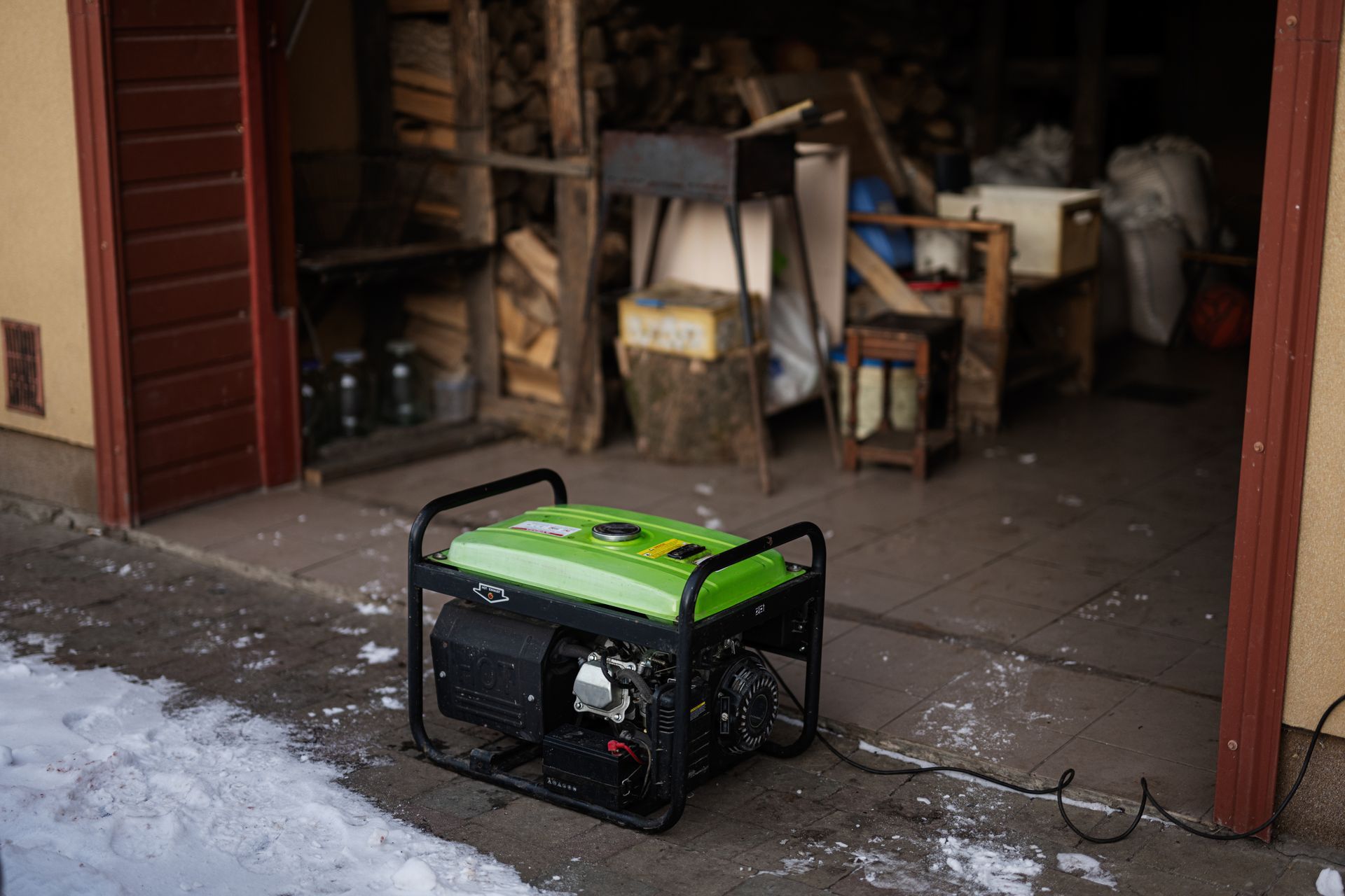Portable green generator on a wet garage floor beside a cluttered open workshop.