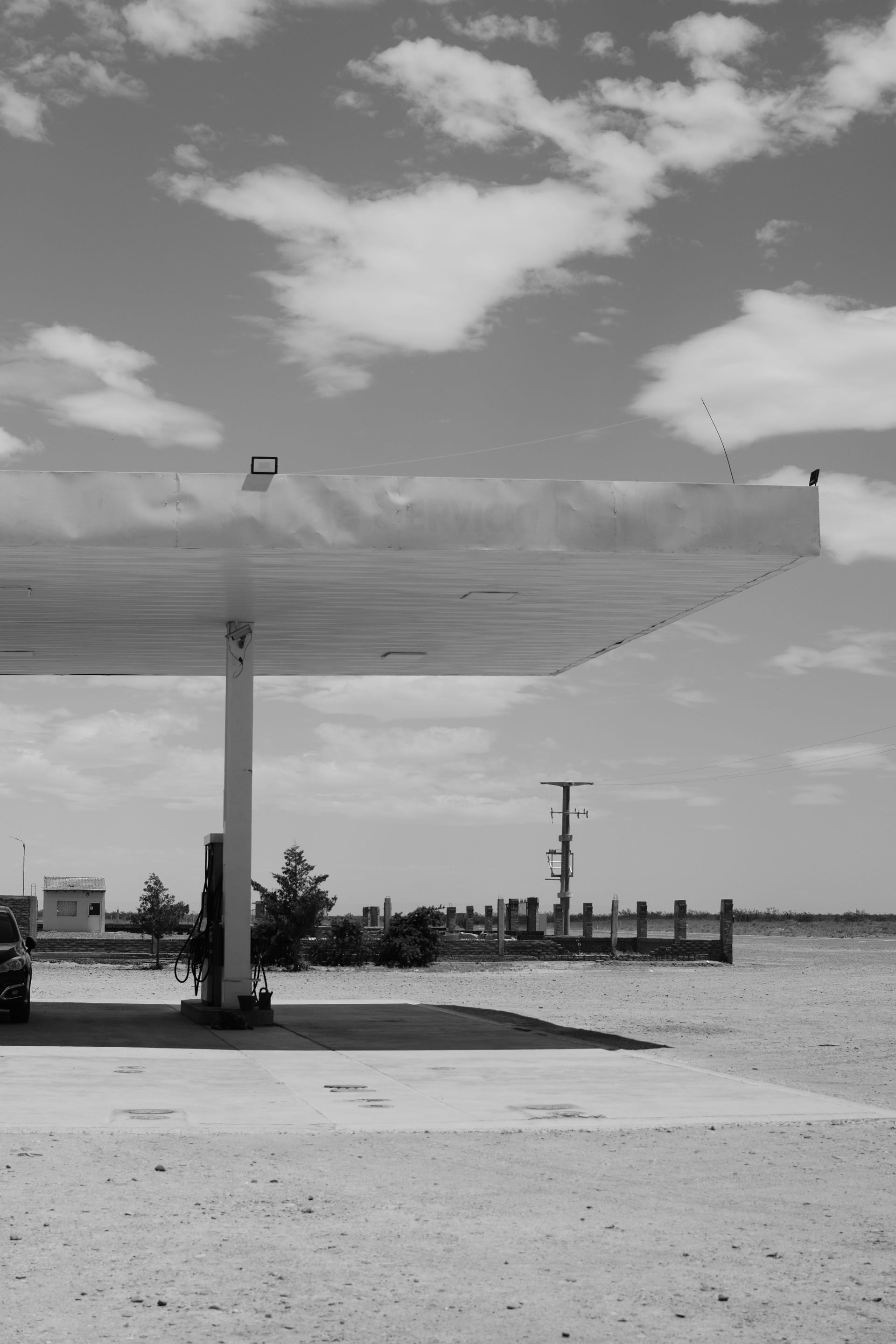Gas station canopy by a waterfront under a cloudy sky, with a pier in the distance.