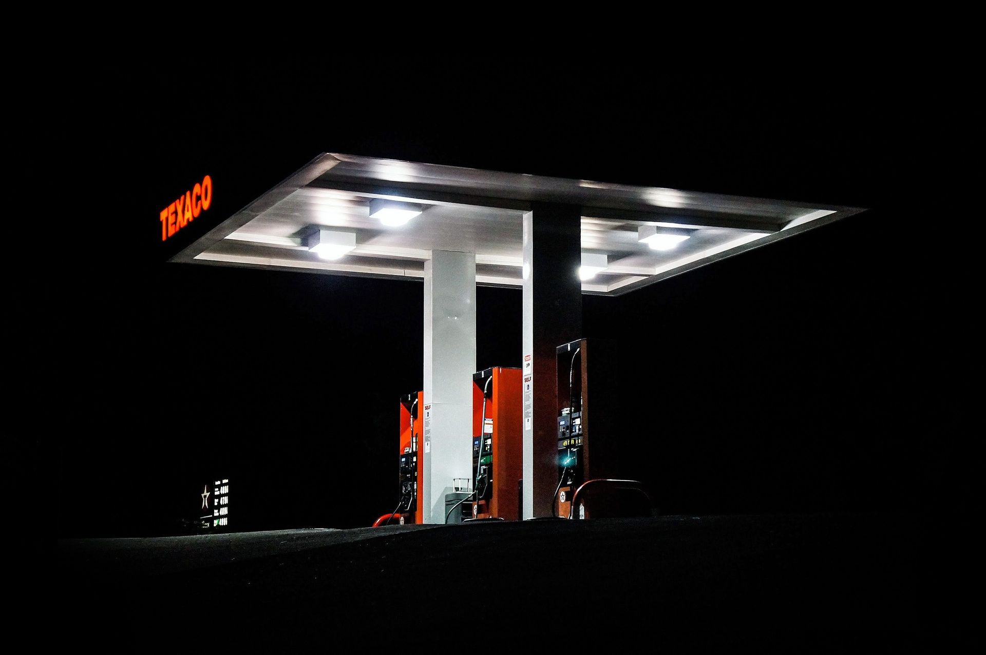 Illuminated gas station canopy at night with red signage and fuel pumps against a dark background
