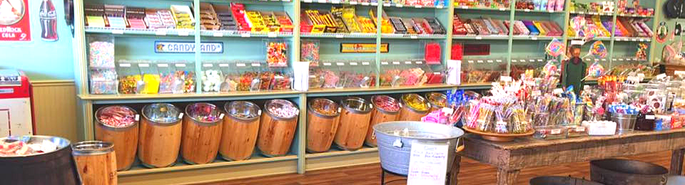 Colorful candy shop counter with jars, shelves of sweets, and wooden barrels under bright display lights