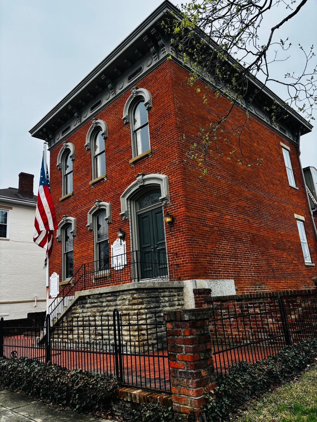 A large red brick building with stairs leading up to it and an american flag flying in front of it.