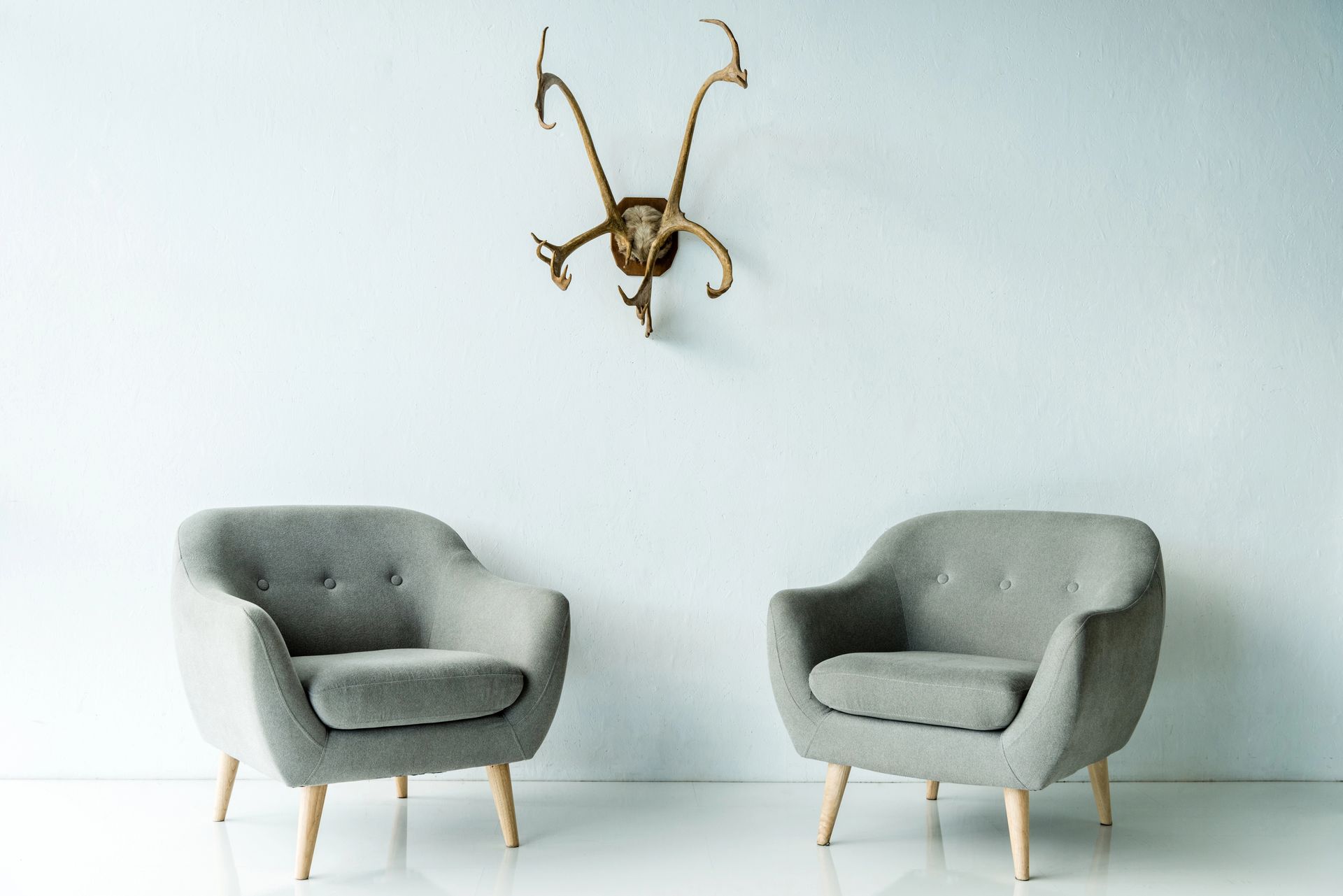 Due poltrone grigie sotto una scultura a forma di corna dorate in una stanza minimalista bianca