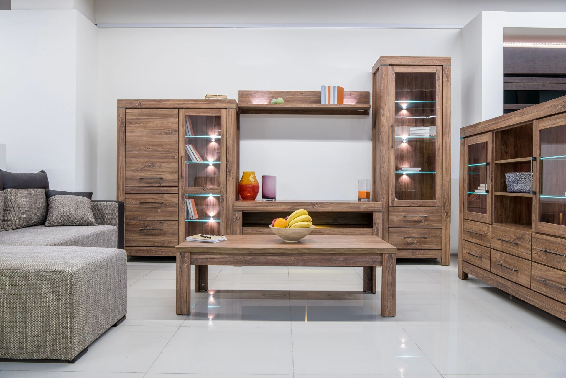 Set da soggiorno in legno con mobile porta TV, armadietti, tavolino da caffè e divano beige su pavimento in piastrelle bianche.
